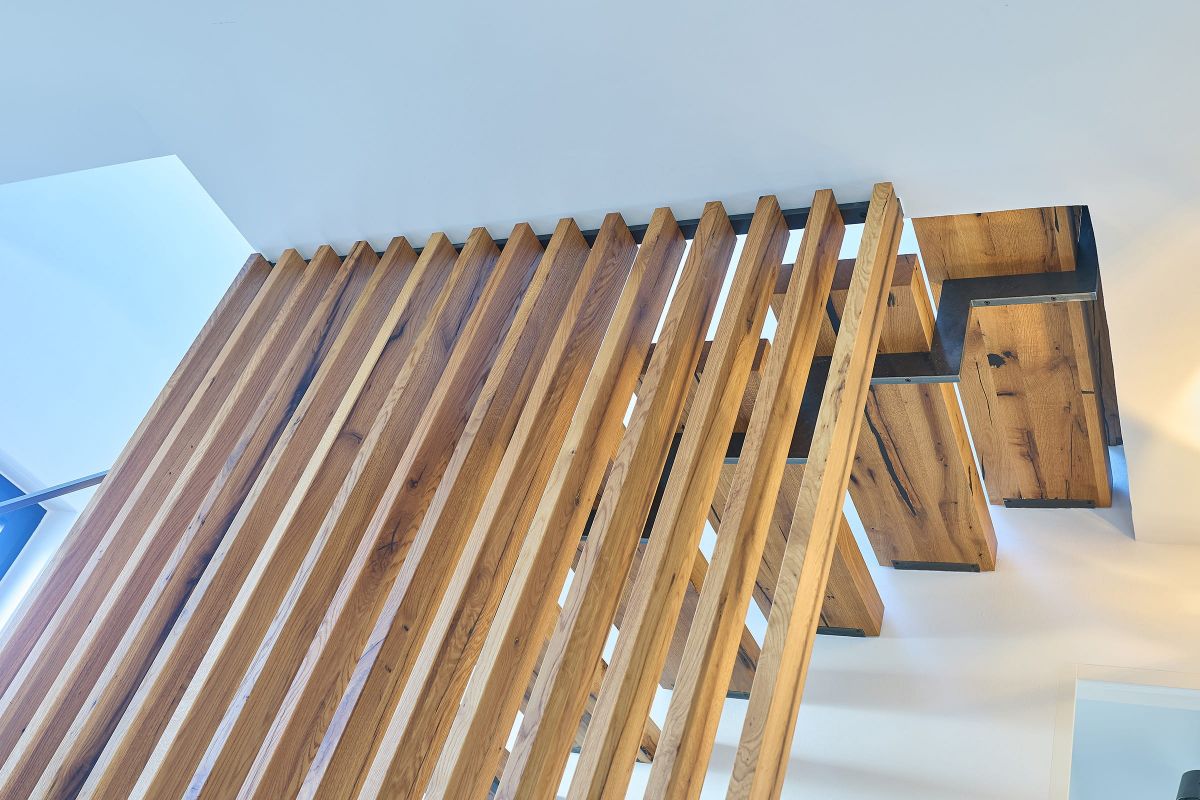 Moderne Treppe aus massivem Holz mit seitlichen Metallwangen und vertikalem Holzgeländer in offenem Raumkonzept.
