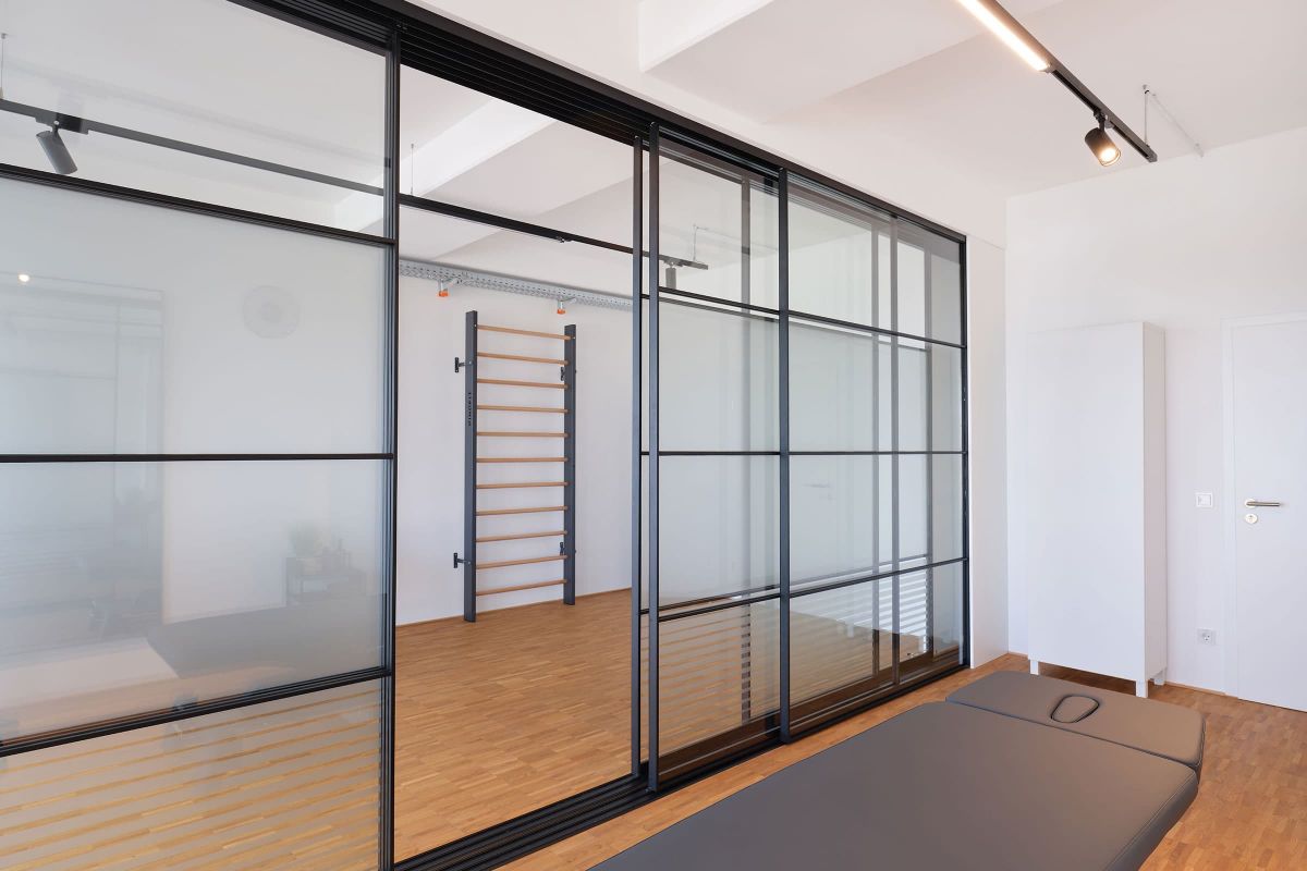 Moderner Behandlungsraum mit Glaswand und klarer Gestaltung im Rahmen einer maßgeschneiderten Praxisausstattung