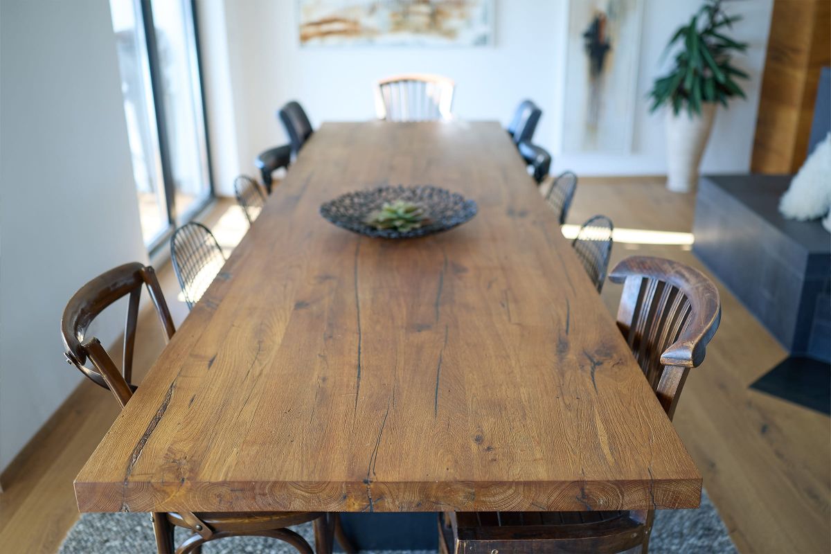 Detailaufnahme eines großen, massiven Esstisches aus Holz mit charaktervoller Maserung und verschiedenen Stühlen im modernen Wohnraum.