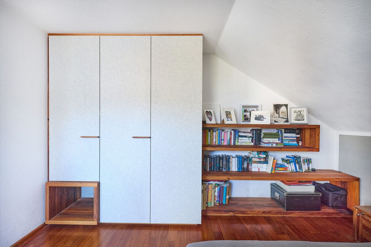 Einbauschrank und maßgefertigtes Regal unter der Dachschräge mit Holzdetails, Büchern und persönlichen Accessoires.