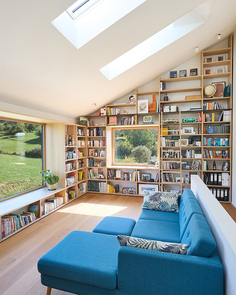 Stillvolles Dachgeschoss mit großem Fenster und eingepassten Wandregal unter der Dachschräge, hinreichend zu einer Sitzbank vor dem Fenster.