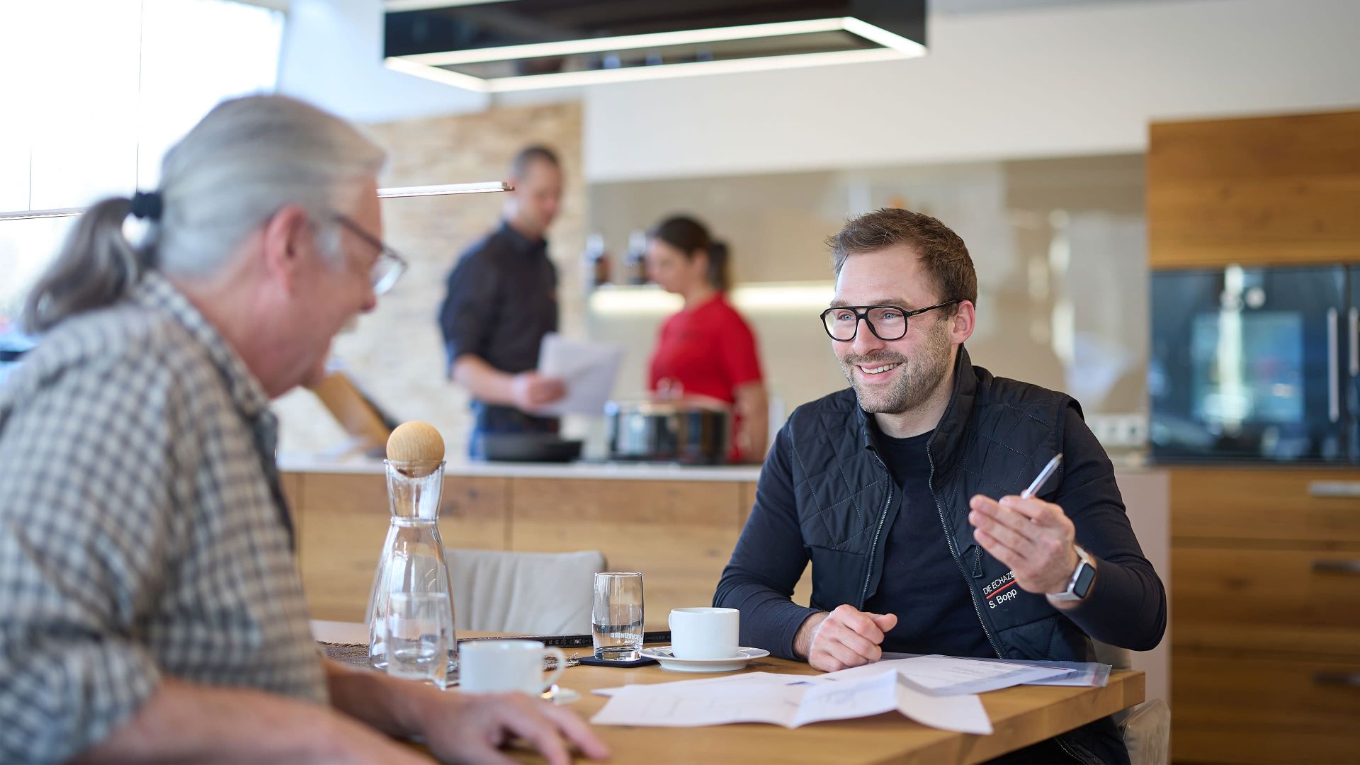 Ein freundlicher Mitarbeiter von ECHAZ erklärt einem Kunden ein Konzept, im modernen Küchenumfeld mit lockerer Atmosphäre.