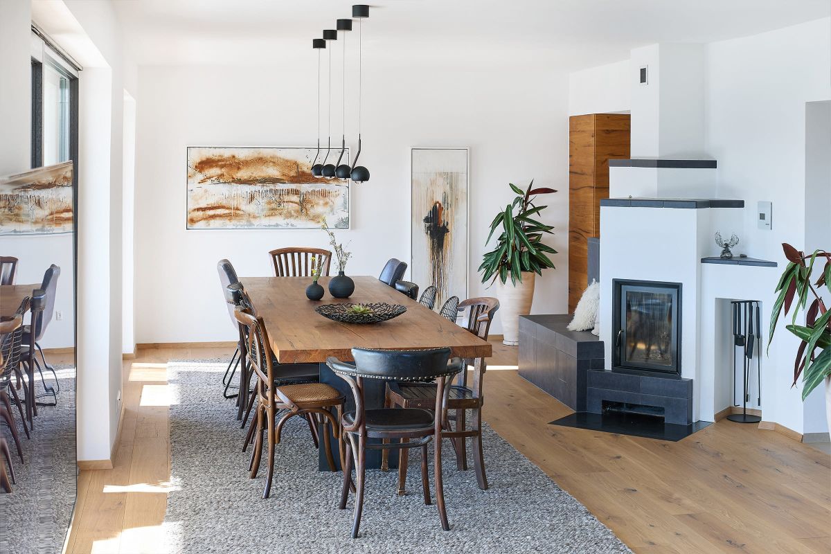 Moderner Wohn- und Essbereich mit großem Holztisch, Kamin, Pflanzen und natürlichem Licht in stilvollem Ambiente.