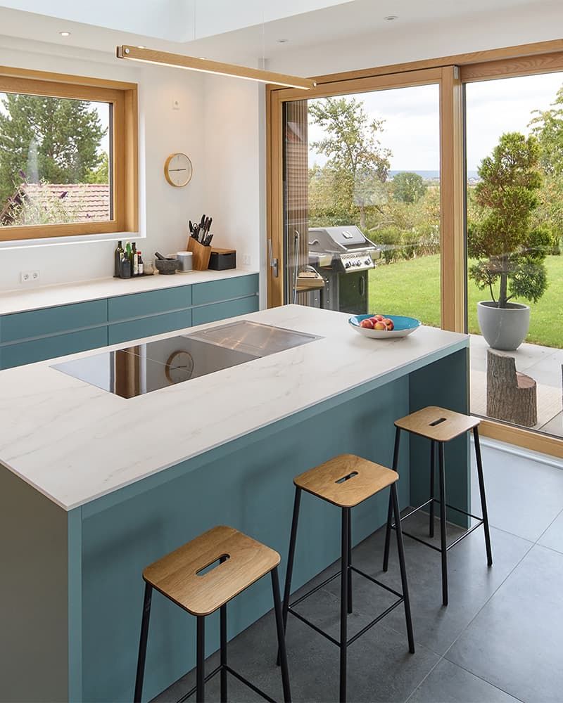 Freistehende Kücheninsel mit eingelassenem Kochfeld und edlen Barhockern davor.